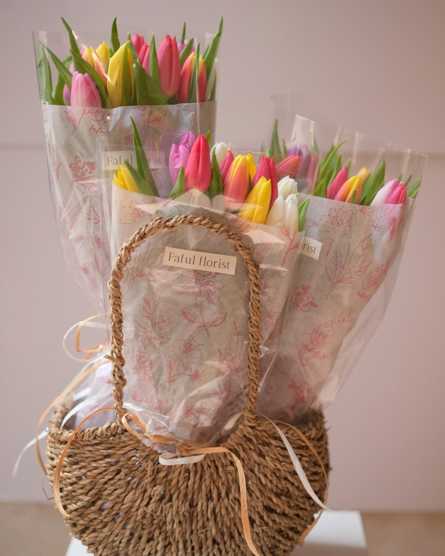 Mixed color tulip bouquets in wicker baskets with floral paper wrapping, front close-up by Faful Florist