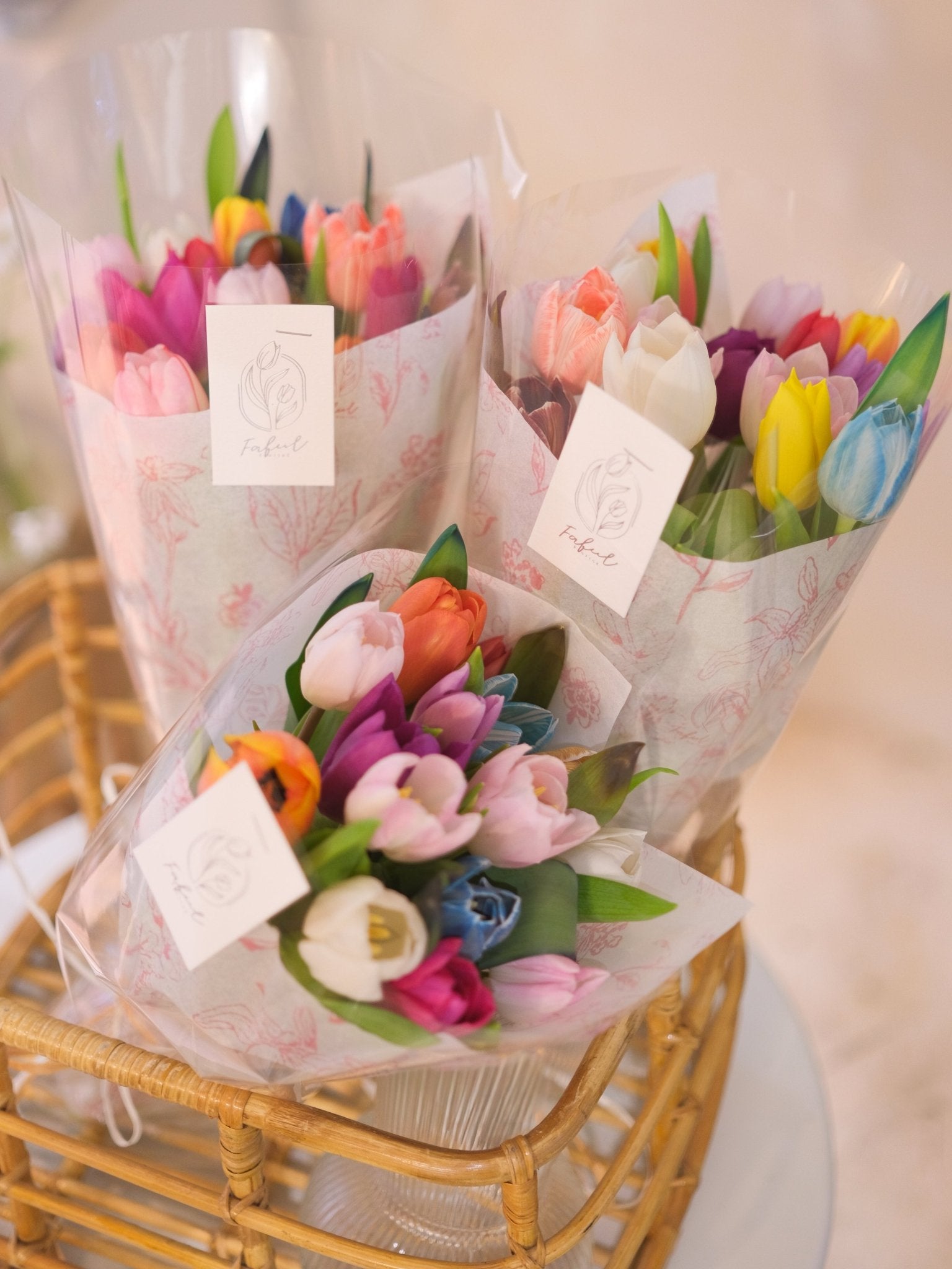 Mixed rainbow tulip bouquets in wicker baskets with pink floral wrapping, close-up by Faful Florist