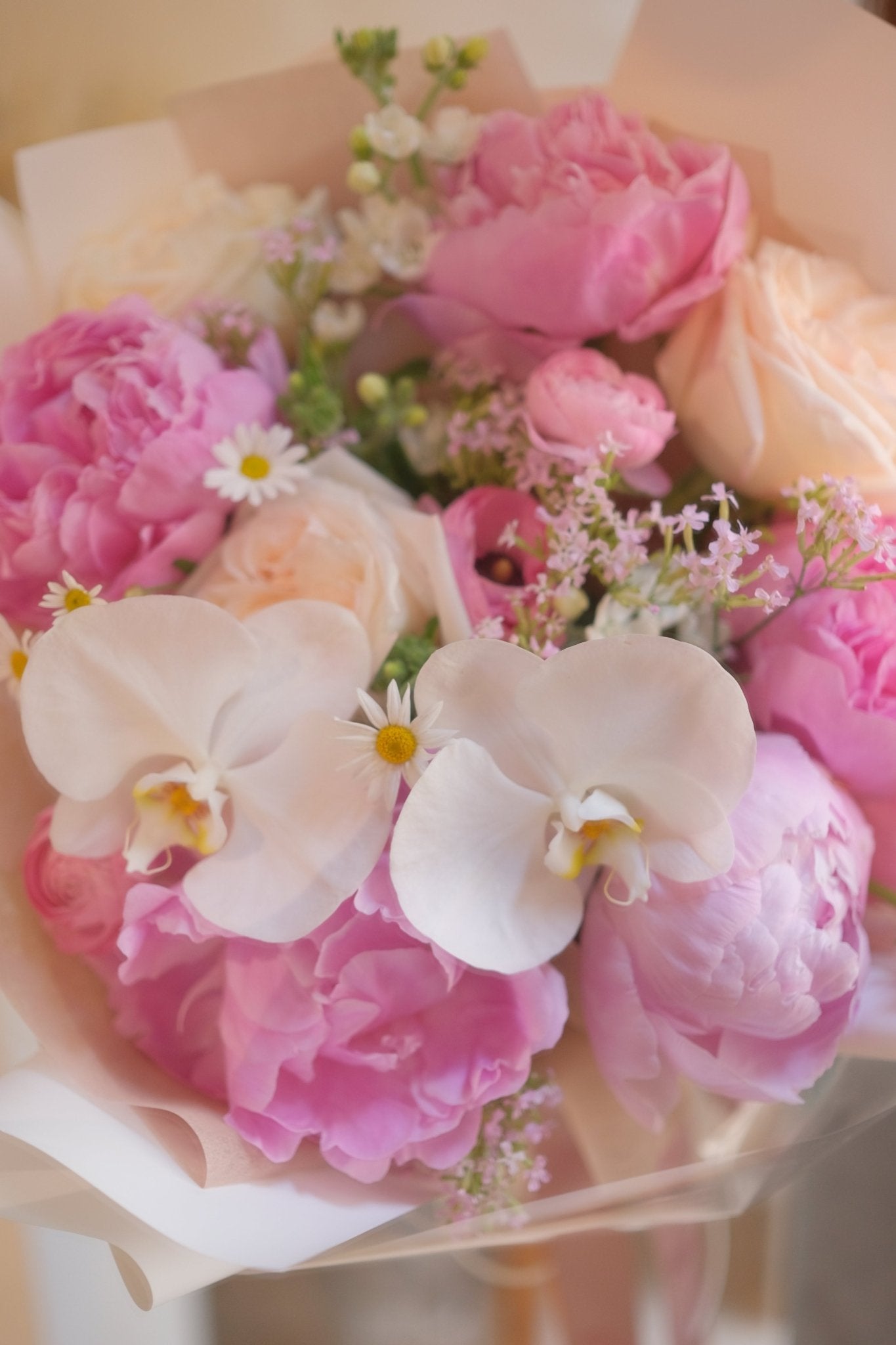 Pink peony and white orchid bouquet with translucent wrapping on wood by Faful Florist