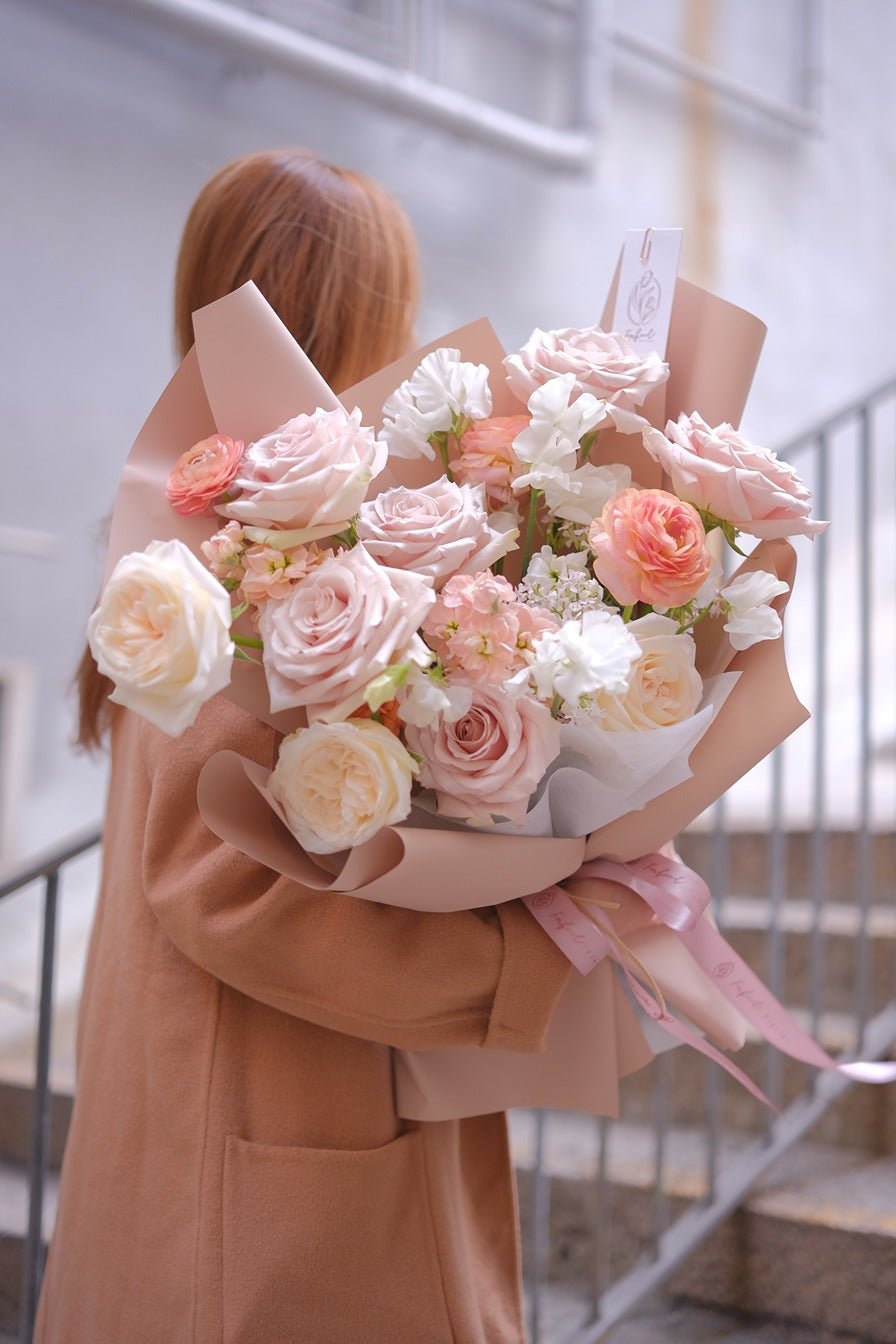 Pastel pink and peach rose bouquet with white filler in pink kraft paper by Faful Florist